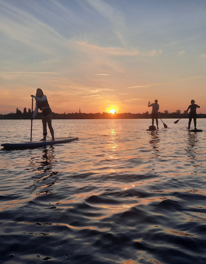 3 mensen op supboards tijdens ondergaande zon