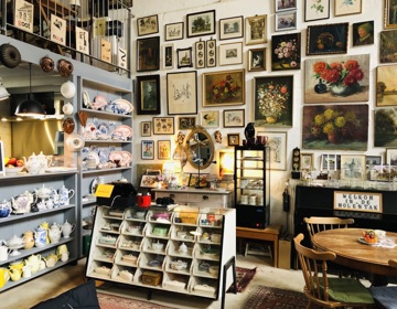 winkeltje vol met snuisterijen en oude spulletjes zoals schilderijen van stillevens en servies