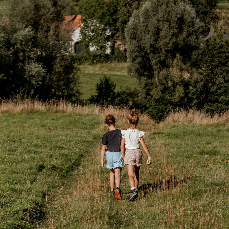 Twee meisjes wandelen een heuvel af met uitzicht op een oude hoeve