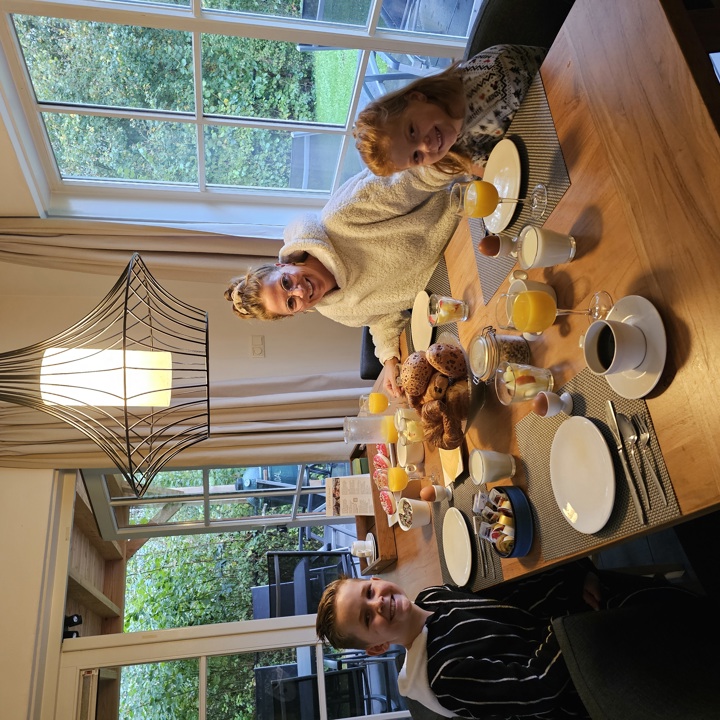 Een moeder en twee kleine kinderen zitten aan tafel van hun vakantiehuisje voor een lekker ontbijtje