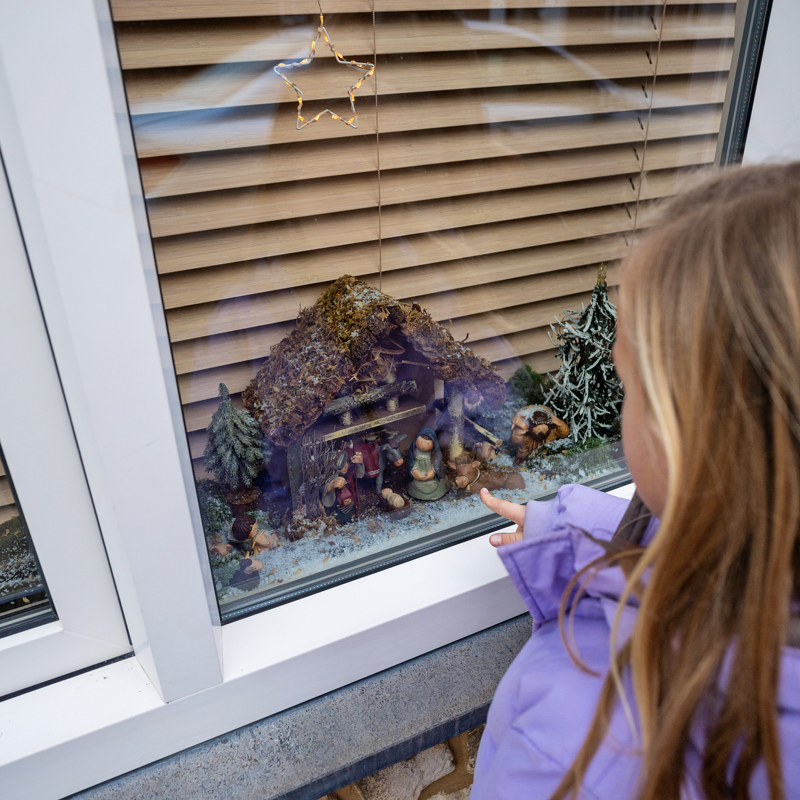Meisje kijkend naar klein kerstkribke achter het raam