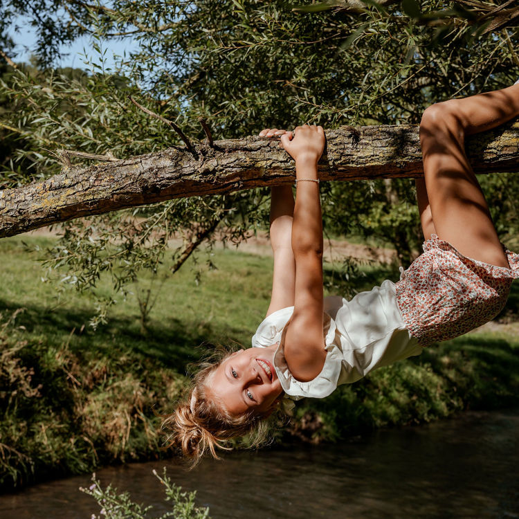 Meisje hangt als een koala aan een laaghangende boomstam boven de Geul. 