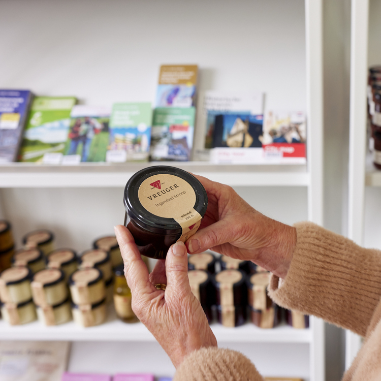 Mevrouw houdt een potje stroop vast in een winkel vol met streekproducten.