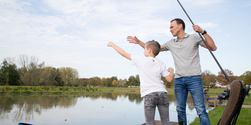 Vader en zoon in de weer met een vishengel langs de visvijver in Valkenburg. 