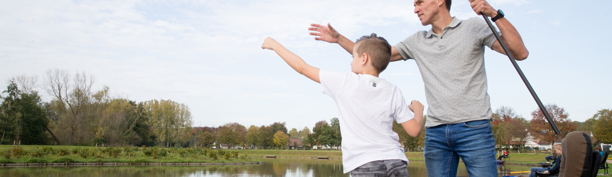 Vader en zoon in de weer met een vishengel langs de visvijver in Valkenburg. 
