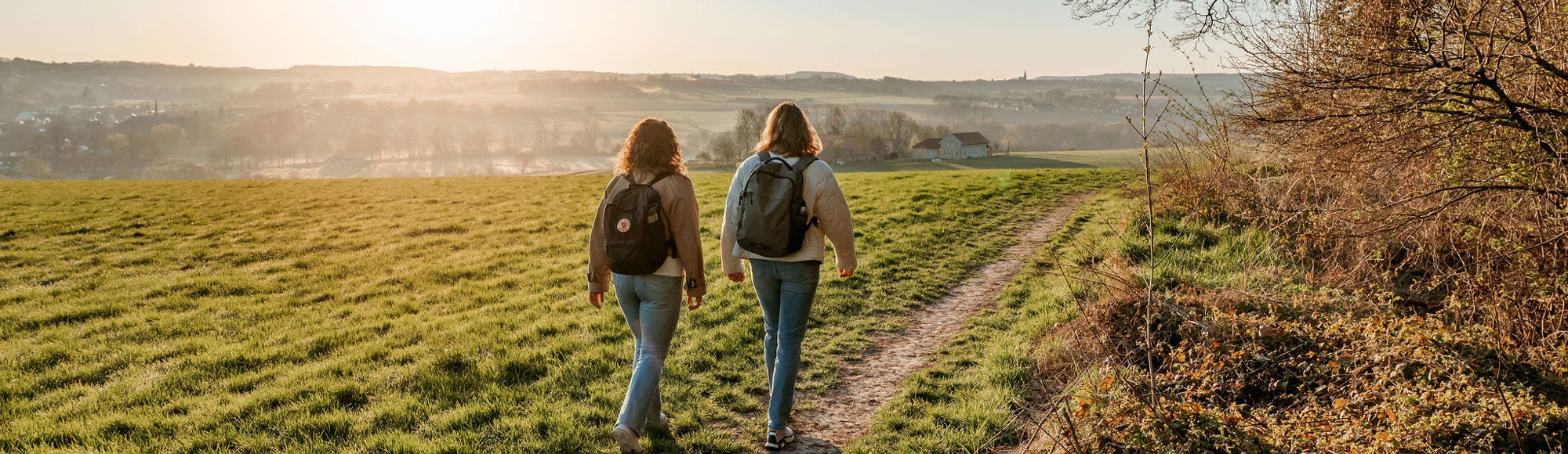 Twee meiden met rugzak aan het wandelen door een weiland met uitzicht