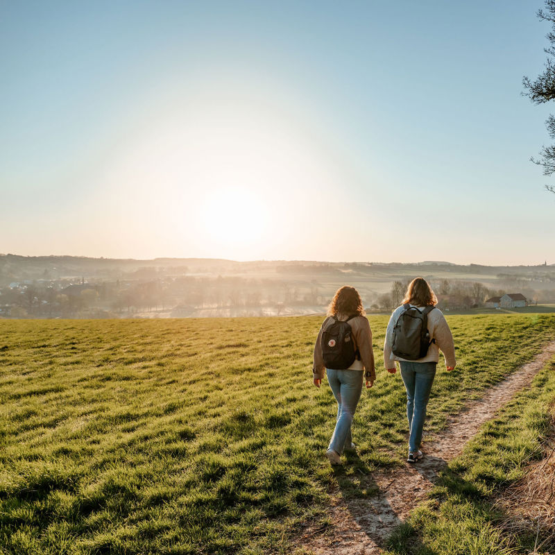 Twee meiden met rugzak aan het wandelen door een weiland met uitzicht