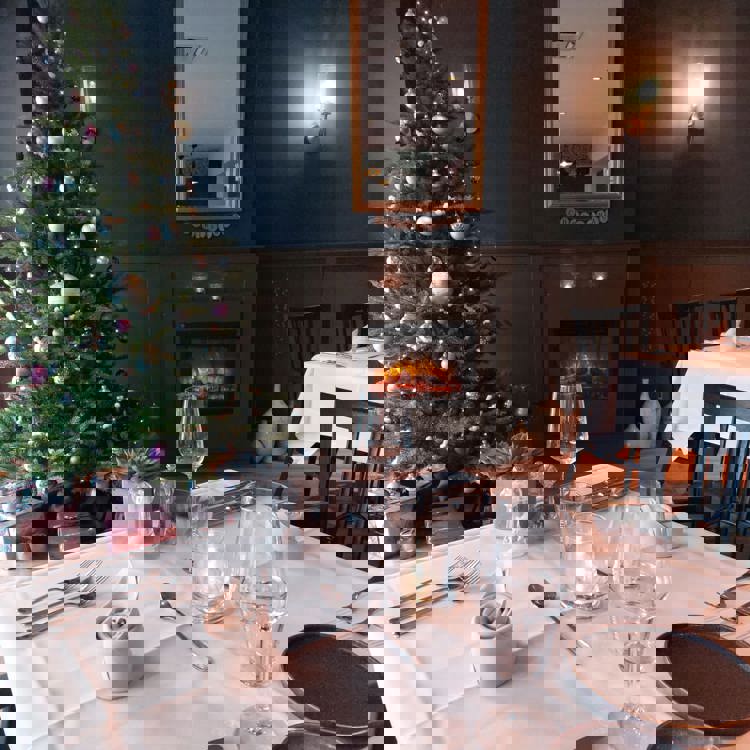 Gedekte tafel in restaurant met een kerstboom en openhaard op de achtergrond.