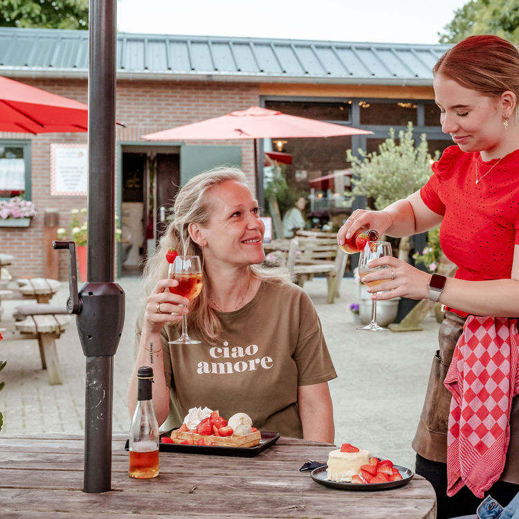 Twee vriendinnen genieten van aardbeiensecco op het terras met een aardbeiendessert. 