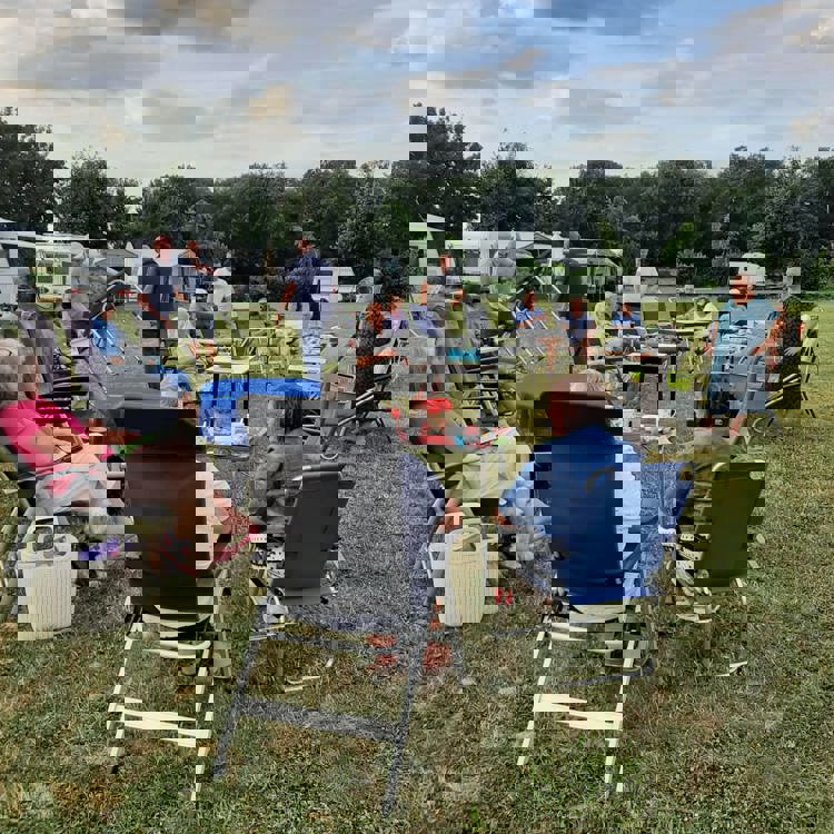 Een hoop campinggasten verzamelen zich bij elkaar met tafels en stoelen. 