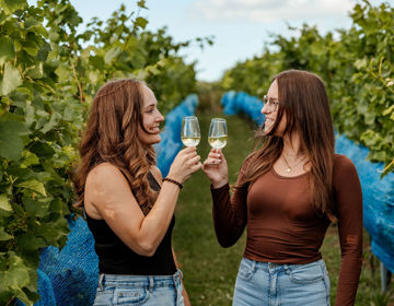 Twee vrouwen proosten tussen de wijnranken met een glas lokale witte wijn.