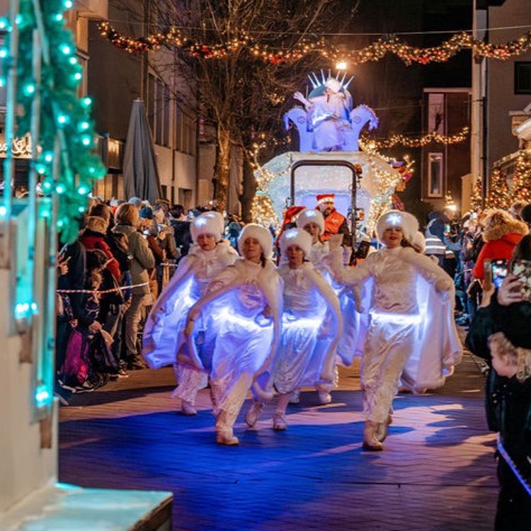 Groep danseressen in wit verlichte kostuums voor de praalwagen met daarop de Ice Queen tijdens de Parade van Kerststad Valkenburg