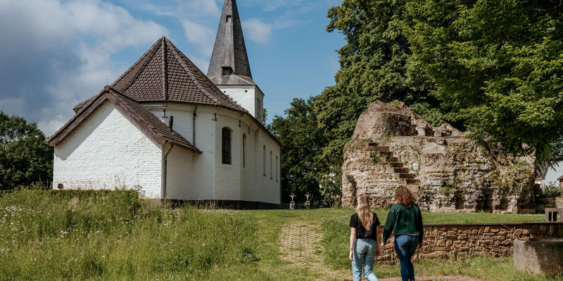 Twee dames wandelen richting een klein wit kerkje. 