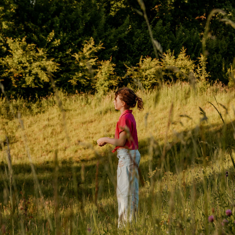 Meisje in het weiland met een roze blouse en een spijkerbroek aan de bosrand