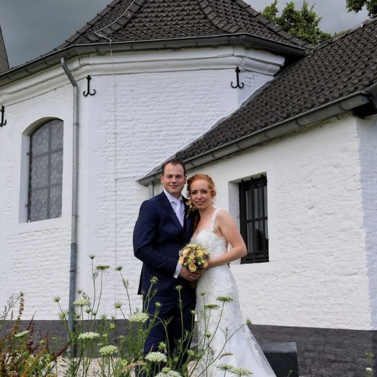 Bruidspaar poseert voor een wit kerkje. 