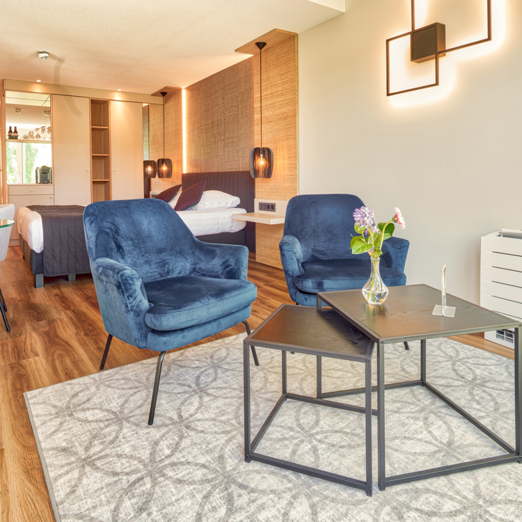 Hotelkamer met gezellig zitje en op de achtergrond een luxe hotelbed.