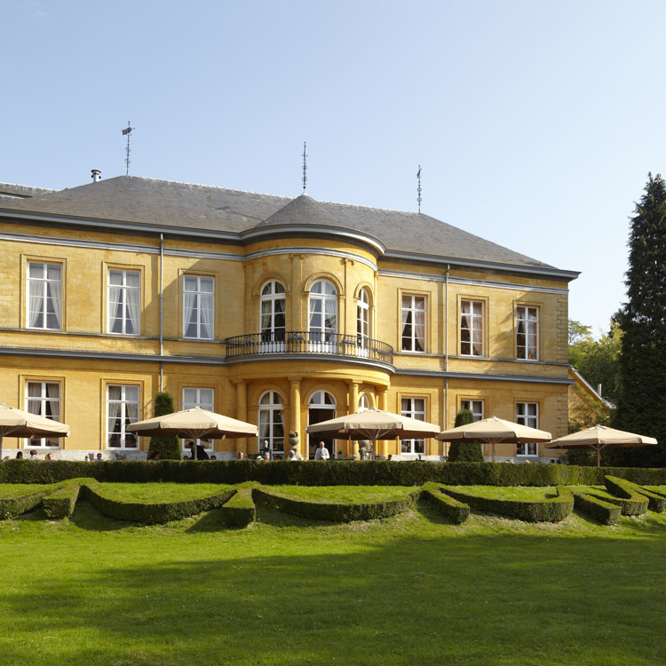 Okergeel gekleurd kasteel omringd door een prachtige kasteeltuin met parasols. 