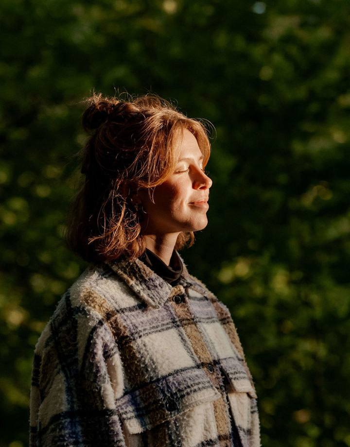 Jonge vrouw geniet van de avondzon op haar gezicht in een natuurrijke omgeving.