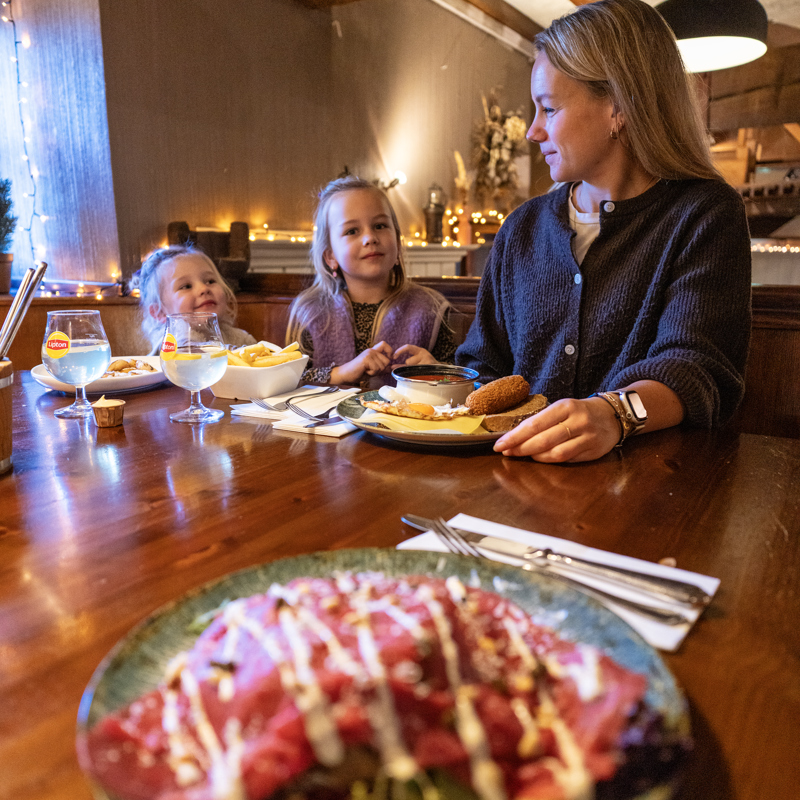 Bord met gerecht en vrouw en kinderen in achtergrond