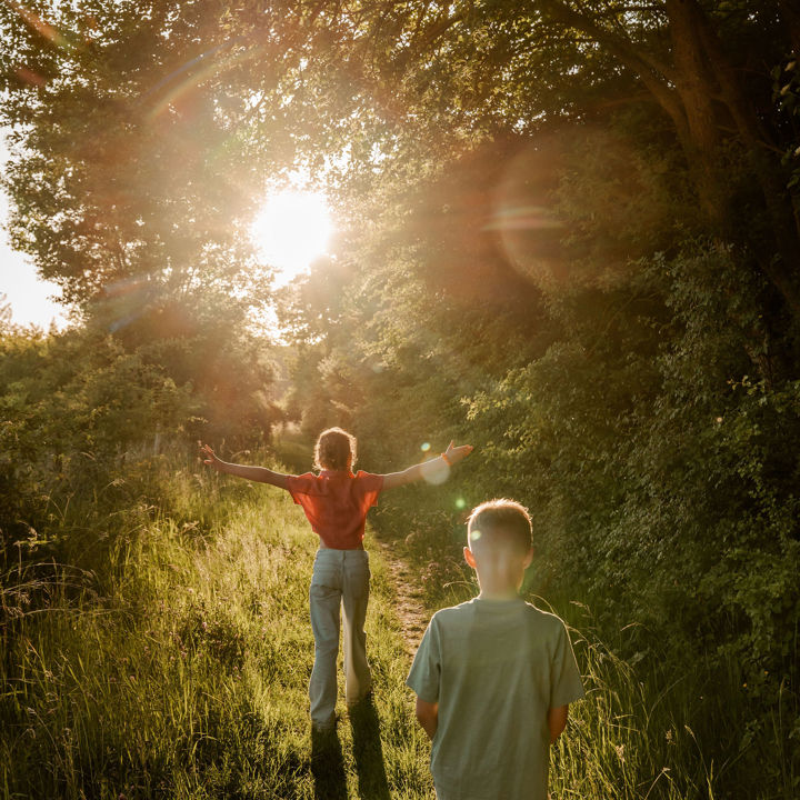 Twee kinderen achter elkaar aan het wandelen langs de bosrand bij zonsondergang