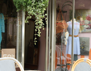 Een etalage met daarin een paspop met een lichtblauw jurkje en een camel kleurige riem.